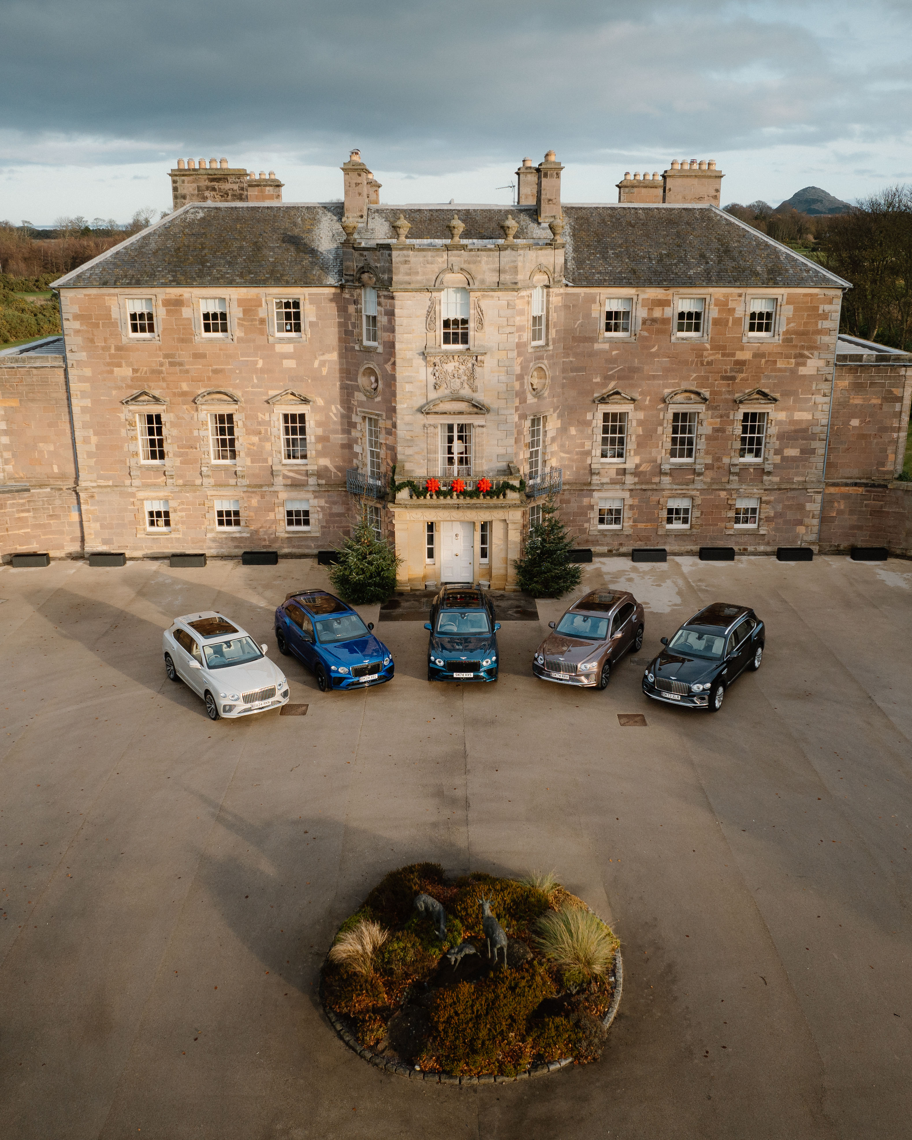 Aerial shot of five Bentleys parked in a semicircle outside a stately home